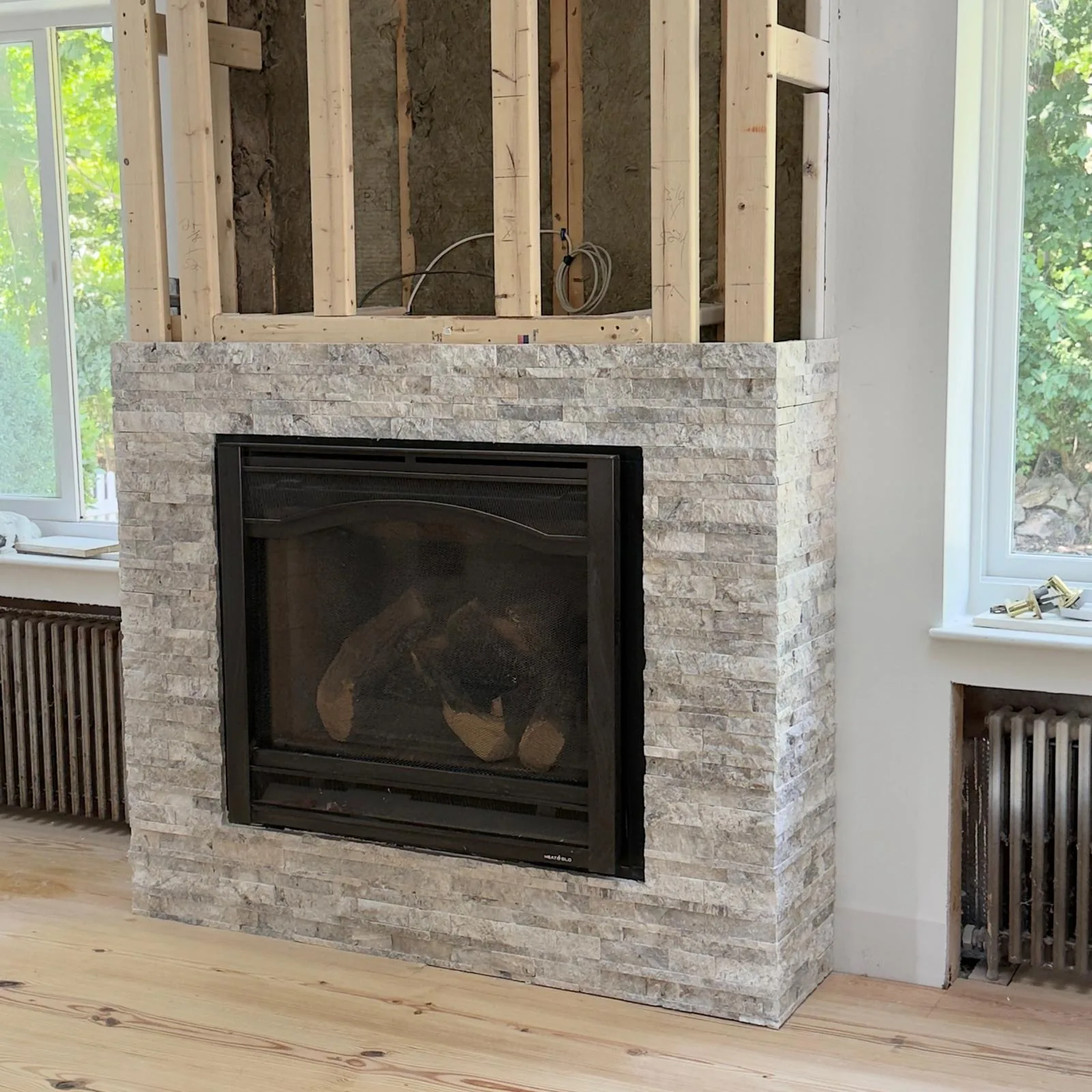 Stone veneer around a fireplace with exposed wall framing above